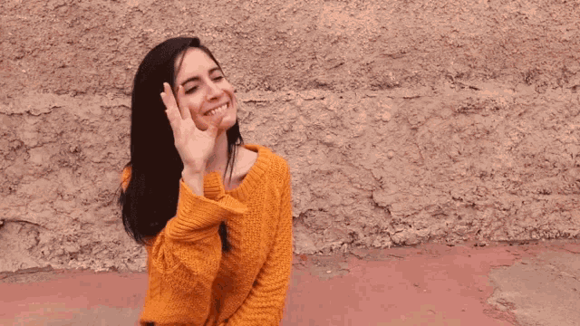 a woman in an orange sweater covering her mouth with her hands