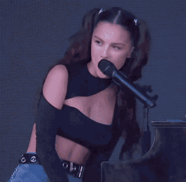 a woman is singing into a microphone while wearing a black crop top .