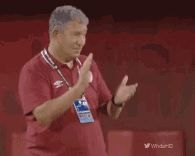 a man in a maroon shirt applauds in front of a twitter header