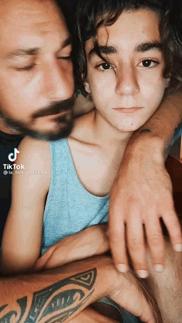 a man with a tattoo on his arm is hugging a boy