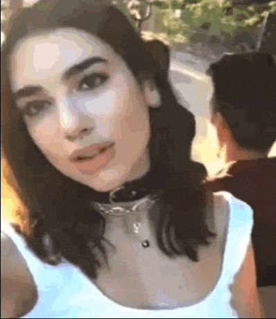 a woman wearing a choker and a white tank top looks at the camera