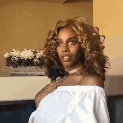 a woman with curly hair wearing a choker and a white off the shoulder top