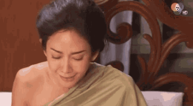 a woman is sitting on a bed with her eyes closed and a green cloth on her shoulders .