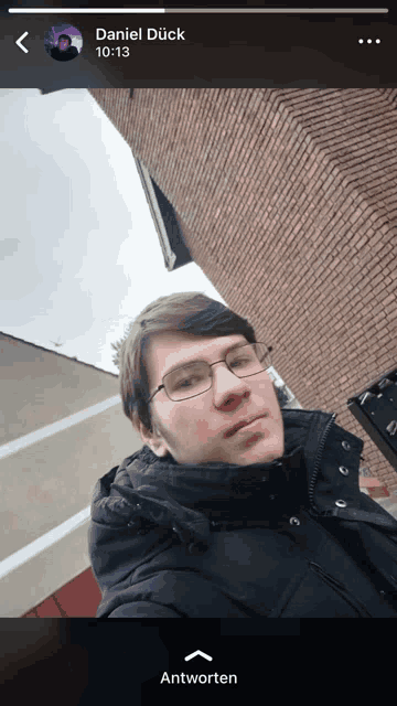 a man wearing glasses and a black jacket is standing in front of a brick building