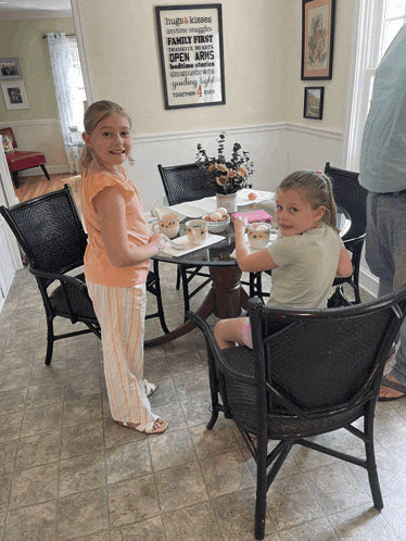 two young girls sitting at a table with a sign on the wall that says hugs and kisses
