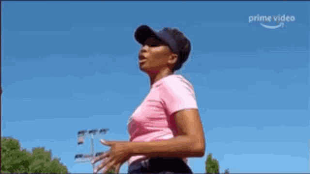 a woman in a pink shirt and black hat is running on a tennis court .