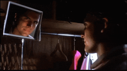 a man looks at himself in a mirror in a dark room