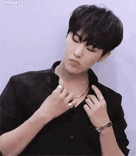 a young man wearing a black shirt and a bracelet is adjusting his collar .