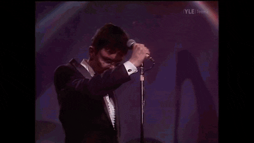 a man in a tuxedo is singing into a microphone while wearing glasses .