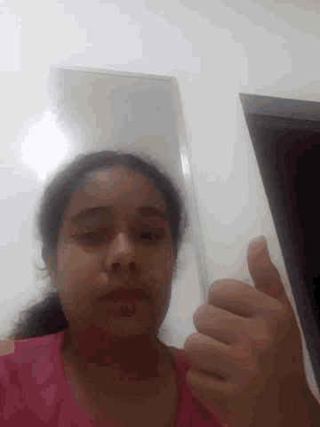a girl in a pink shirt is giving a thumbs up in front of a mirror