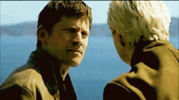 two men are looking at each other while standing in front of a body of water .