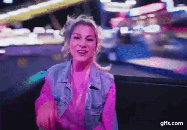 a woman in a pink sweater and a denim jacket is sitting in a chair and smiling .