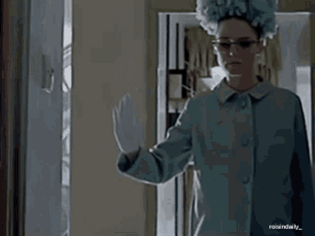 a woman wearing glasses and a blue wig is standing in front of a door .