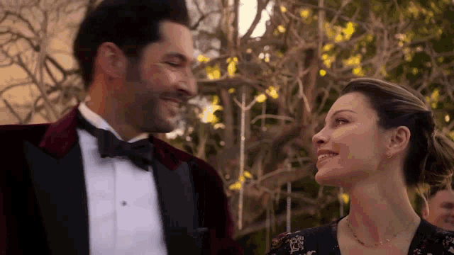 a man in a tuxedo and a woman in a dress are smiling at each other .