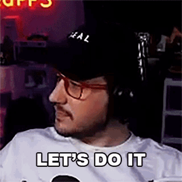 a man wearing headphones and a hat is sitting in front of a microphone and says let 's do it .