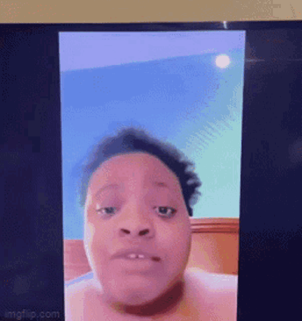 a woman without a shirt is looking at the camera on a tv screen .