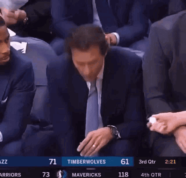 a man in a suit and tie sits in the stands watching a game between the timberwolves and mavericks
