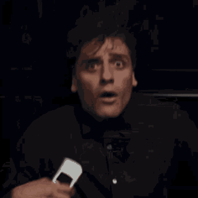 a man in a black shirt is making a funny face while holding a microphone in his hand .