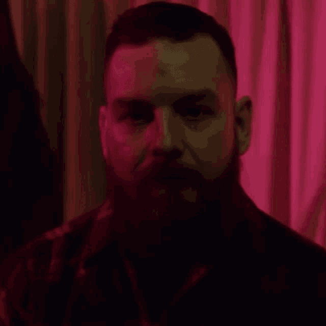 a man with a beard is looking at the camera in a dark room