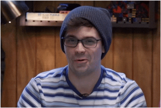 a man wearing glasses and a beanie is sitting in front of a wooden wall