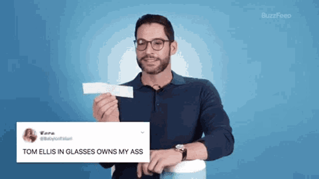 a man is holding a piece of paper that says tom ellis in glasses owns my ass .