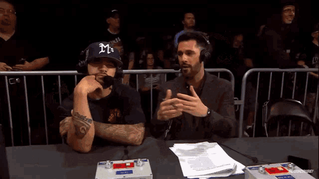 a man named trev miguel is sitting at a table with a microphone