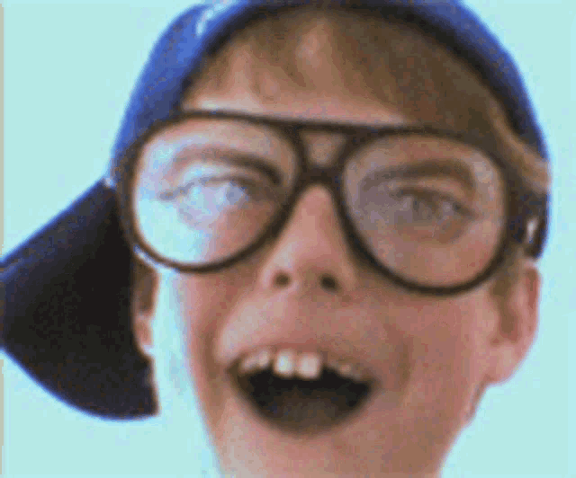 a young boy wearing glasses and a baseball cap is making a funny face