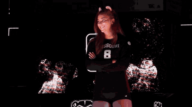 a girl wearing a missouri number 8 jersey stands with her arms crossed