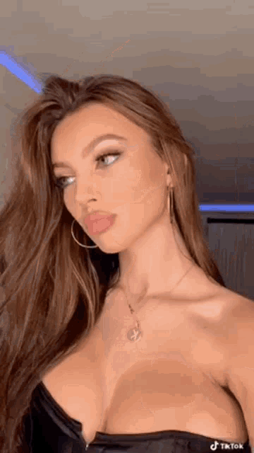 a woman in a black strapless top and necklace is looking at the camera .