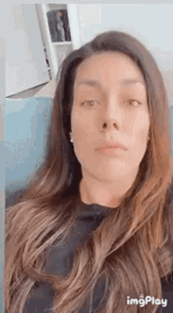 a woman with long hair is sitting on a couch and looking at the camera .