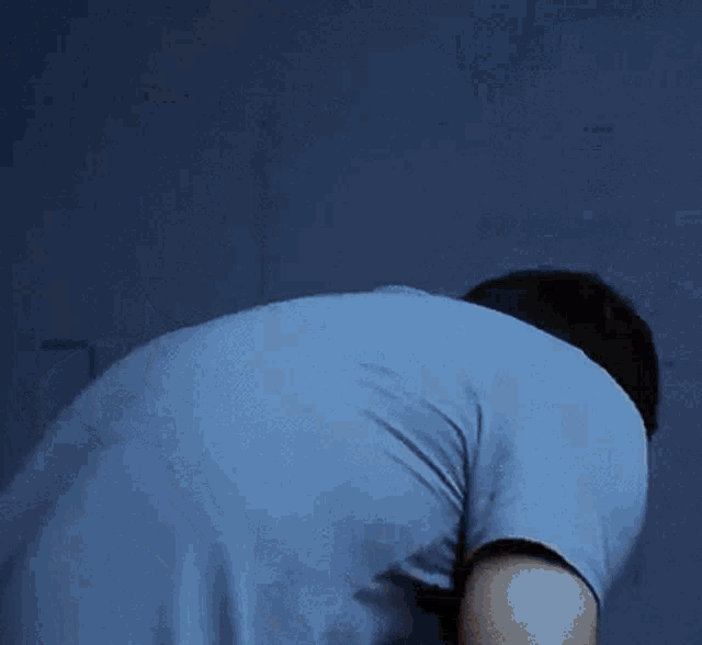 a man in a blue shirt is kneeling down in front of a wall .