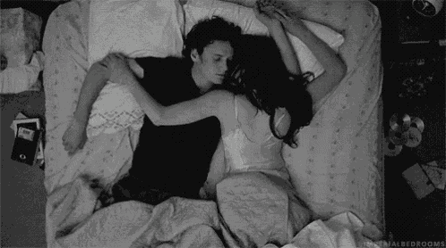 a black and white photo of a man and woman sleeping in bed .