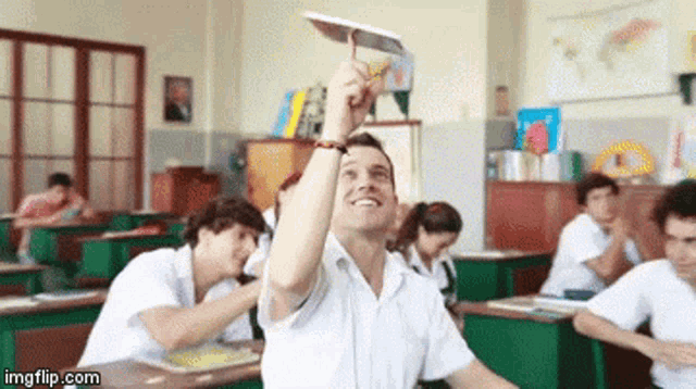 a man in a classroom is holding a paper airplane in his hand