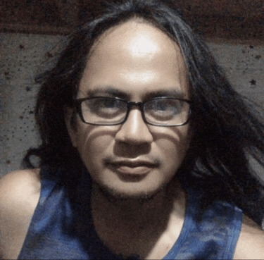a man with long hair and glasses looks at the camera