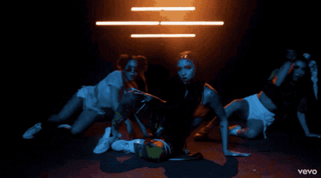 three women are dancing in a dark room with the word vevo on the bottom right