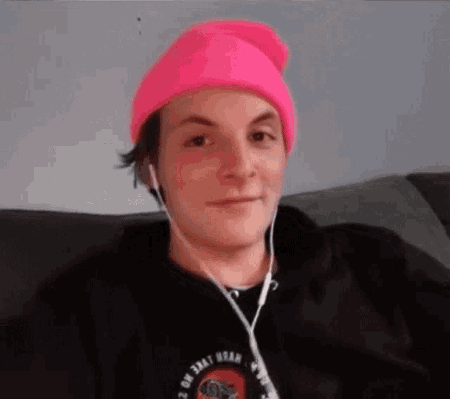 a man wearing a pink hat and earbuds is sitting on a couch .