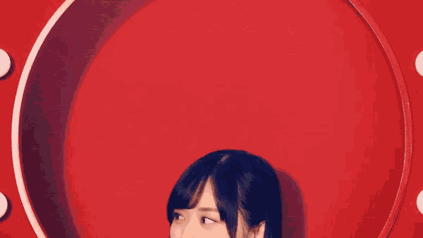 a woman stands in front of a red wall with a white circle in the middle