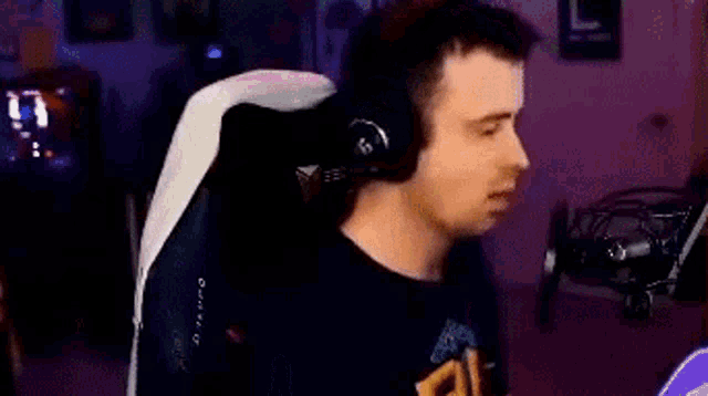 a man is sitting in a gaming chair wearing headphones and a black shirt .