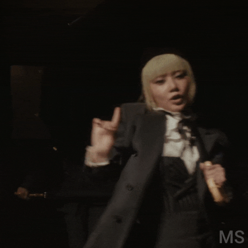 a woman in a suit is holding an umbrella with the letters ms visible in the corner