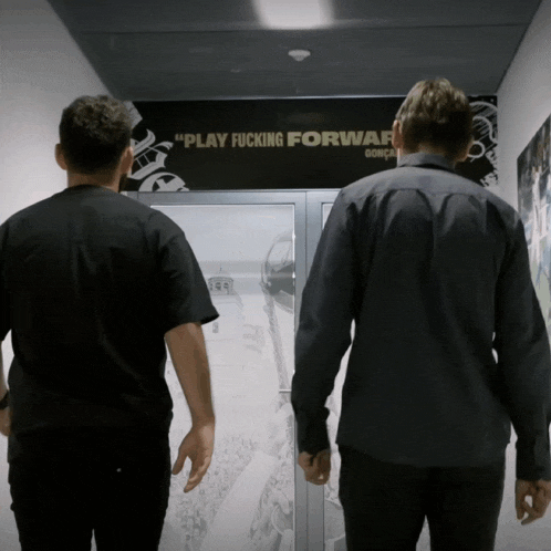 two men standing in a hallway with a sign that says play fucking forward