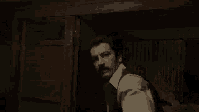 a man with a mustache is standing in a dark room looking at something .