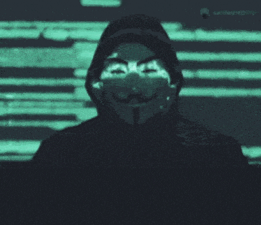 a man wearing a mask and a hood is standing in front of a screen .