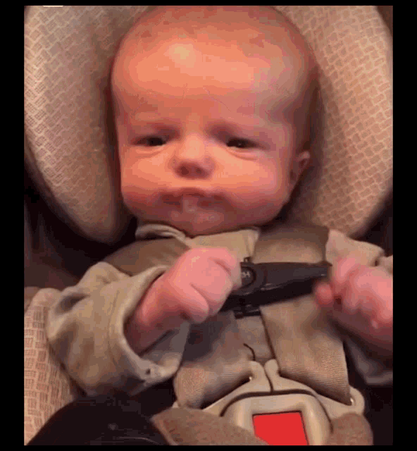 a baby is sitting in a car seat with a red button on the seat belt
