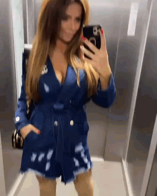 a woman in a blue dress is taking a selfie in an elevator with her phone .
