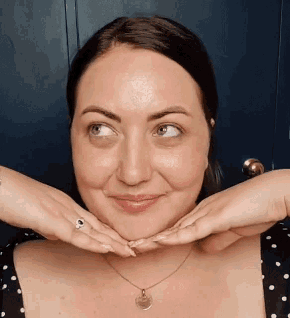 a woman wearing a necklace and a ring is making a funny face with her hands .