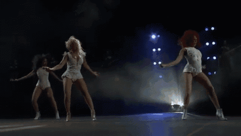 three women are dancing on a stage in front of a crowd