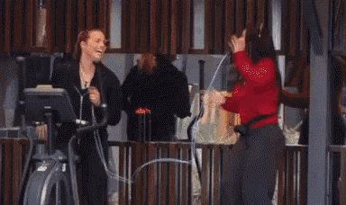 two women are standing next to each other on an elliptical machine and laughing .