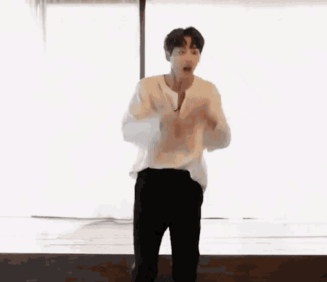 a man in a white shirt and black pants is dancing in front of a window in a room .