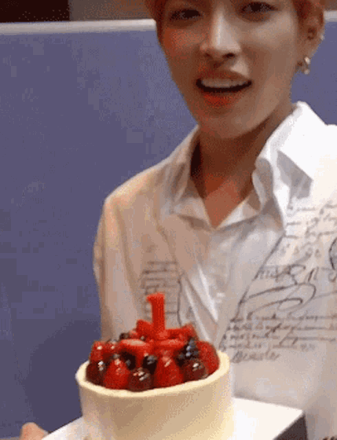 a man is holding a cake with strawberries and blueberries and a number 1 on it .