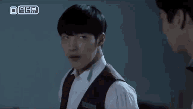 two men are standing next to each other in a dark room and one of them is wearing a vest .